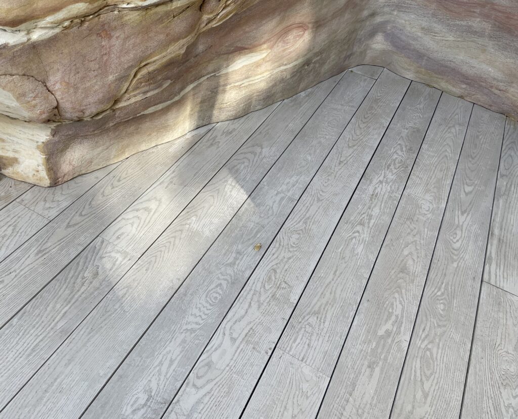 Grey Millboard composite decking scribed around a natural sandstone boulder